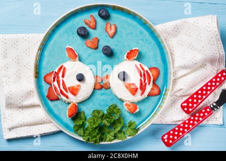 Toasts amusants en forme de poissons baisers, sandwich avec fromage à la crème et baies, idée de nourriture pour les enfants, vue de dessus Banque D'Images