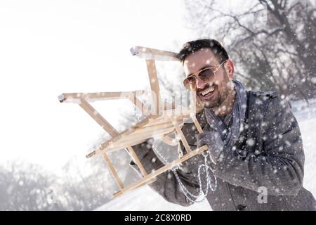 Jeune homme attrayant tenant un traîneau dans un pays merveilleux d'hiver garez-vous pendant les chutes de neige Banque D'Images