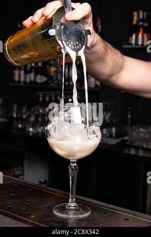 Le barman verse un cocktail moussant dans le verre. Préparation de cocktails au bar du restaurant. Banque D'Images