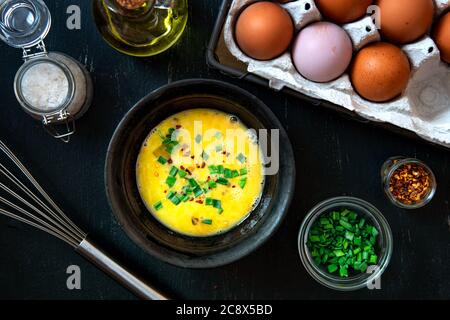 Battre les œufs dans un bol et les ingrédients pour faire une omelette avec des oignons verts. Banque D'Images