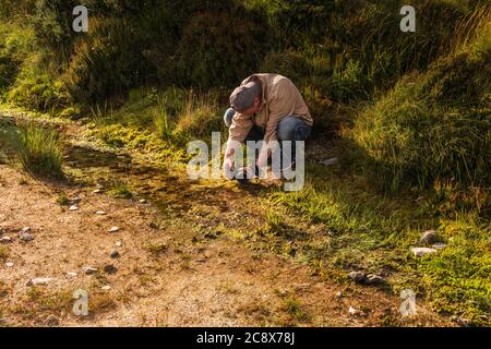 Prise de vue macro. Homme avec un appareil photo pour réaliser des photos macro dans une flaque. Banque D'Images