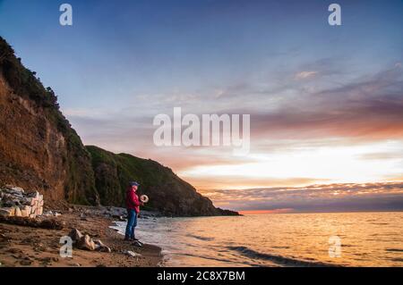 Pêche le matin. Homme avec pêche à la main au lever du soleil sur une plage de mer. Banque D'Images