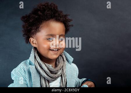 Portrait d'un petit garçon afro-américain habillé de vêtements élégants posant sur fond sombre dans le studio. Modèle bébé. Banque D'Images