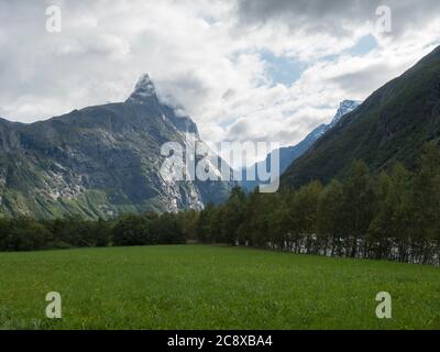 Vue sur le massif de montagne Trolltindene, Troll Wall Trollveggen, la plus haute montagne verticale d'Europe, vallée de Romsdal, Norvège. Herbe verte, ciel bleu Banque D'Images