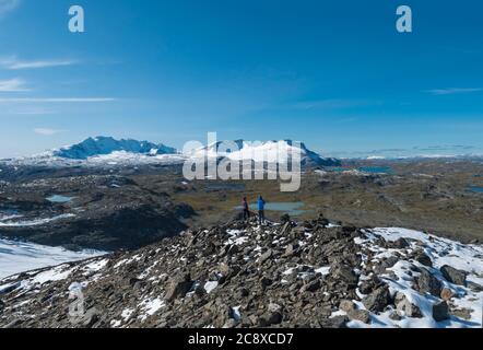 Deux randonneurs se couple en admirant la vue depuis le pied du glacier Smorstabbreen À Krossbu sur les montagnes enneigées et les lacs bleus à Jotunheimen Parc national Banque D'Images