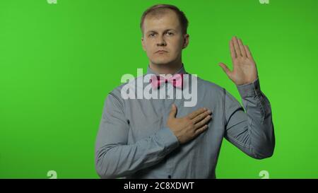 Je jure. Inquiet honnête homme levant la main, se touchant la poitrine et faisant la promesse sincère, prêtant avec une expression responsable. Portrait d'un homme posant sur fond de couleur clé. Émotions des gens Banque D'Images