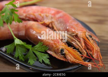 Crevettes crues dans un plateau noir à côté de quelques branches de persil sur une table en bois naturel Banque D'Images