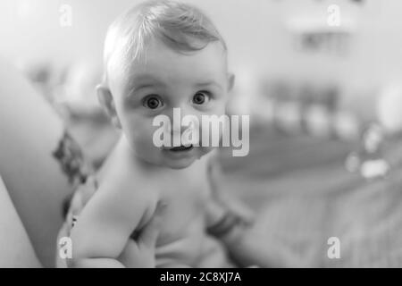 Mère et bébé fils joyeuse intimité. Bébé assis sur le ventre de sa mère et regardant la caméra avec une expression drôle. Portrait en noir et blanc. Banque D'Images