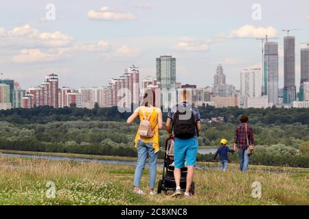 Couple avec bébé bébé en marche sur une colline sur fond de ville d'été et de bâtiments en construction. Loisirs en famille, concept immobilier Banque D'Images