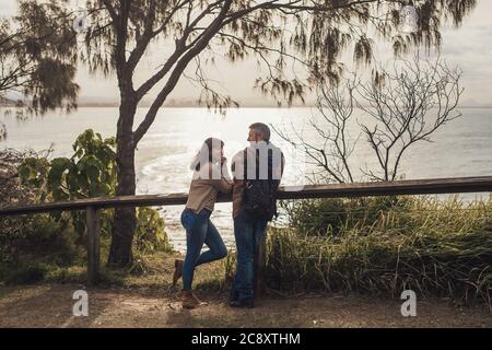 Un couple heureux d'âge moyen, amoureux, séjournez dans un parc avec vue sur l'océan, parlez, regardez les uns les autres et souriez. Banque D'Images