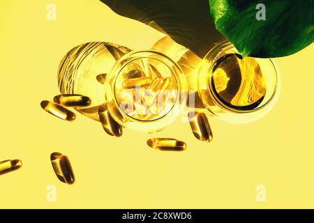 Capsules d'huile de poisson omega-3 et d'huile dans des tasses en verre avec la feuille de monstera sur le fond jaune. Concept de santé et beauté. Banque D'Images