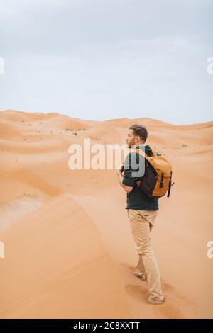 Homme voyage routard au Maroc, désert du Sahara. Explorez la nature africaine, les dunes de sable autour. Vue de derrière. Banque D'Images