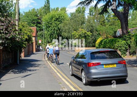 Une voiture passant devant une famille à vélo sur une route tranquille à Shepperton Surrey, Royaume-Uni Banque D'Images