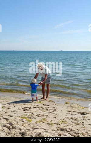 Un père et un fils tout-petits debout sur le bord de l'eau à la plage de Studland Bay, un jour d'été chaud, Dorset Angleterre Royaume-Uni Banque D'Images