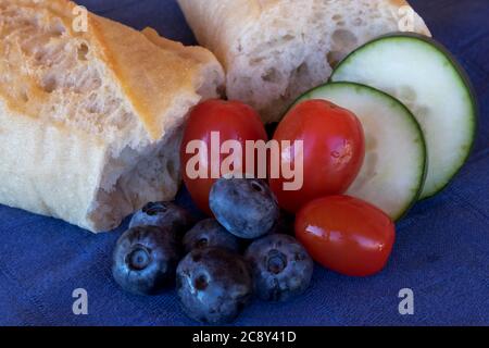 Le pain placé sur une serviette en coton bleu avec des myrtilles, des tomates cerises fraîches et des concombres coupés croquants est une belle collation rustique et saine Banque D'Images