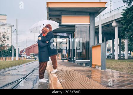 homme femme se couchant sous la pluie. jeune couple ensemble sous un parapluie à un arrêt de transport Banque D'Images