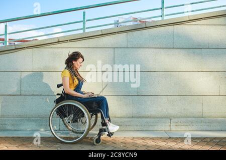 une jeune fille sérieuse marchant avec un fauteuil roulant, plein écran sur le côté photo. copier espace.femme ayant une conversation vidéo, faire un appel vidéo. Banque D'Images