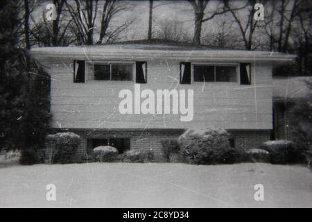 Belle photographie en noir et blanc vintage des années 1970 d'une maison familiale suburbaine commune à deux niveaux recouverte de neige pendant l'hiver. Banque D'Images