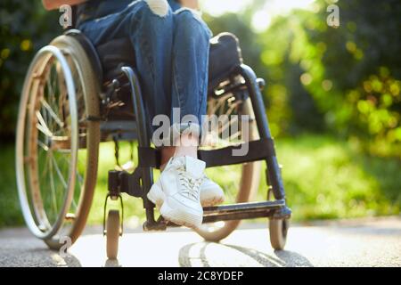 jeune fille handicapée en combinaison et baskets blanches assises avec des jambes croisées sur le fauteuil roulant. photo courte gros plan. Banque D'Images