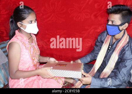 Frère indien et soeur portant un masque protecteur donnant cadeau de festival. Rakhi célébration en inde pendant le covid-19, corona virus concept. Banque D'Images