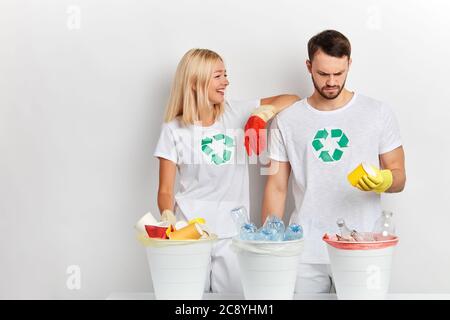 Jeune fille et gars triant des bouteilles en verre, des bouteilles en plastique, des tasses isolées sur blanc. Femme enseignant à son petit ami de recycler les déchets. Portrait en gros plan. l Banque D'Images