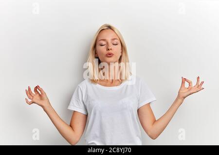 Portrait de magnifique décontracté jeune femme gardant les yeux fermés tout en méditant à l'intérieur, pratiquant yogaa, gardant les doigts dans le geste mudra. Mode de vie, Banque D'Images