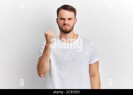 Un jeune homme nerveux en colère montre un poing serré, donnant un avertissement isolé sur fond blanc de studio. Portrait de gros plan, frustration.langage corporel, visage Banque D'Images