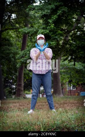 Femme asiatique américaine, probablement chinoise, assiste à un cours de Tai Chi en plein air tout en portant un masque chirurgical et des gants en caoutchouc. À Flushing, Queens, New York Banque D'Images