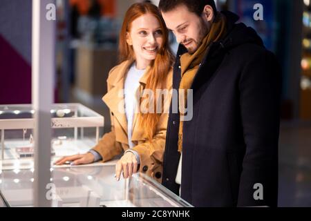 jeune couple caucasien dans le shopping, a décidé d'acheter des bijoux pour la femme dans le centre commercial.excitée redhaired femme et jeune homme barbu ensemble Banque D'Images