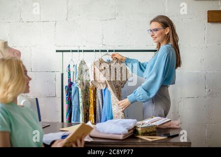 Deux femmes fashion designers travaillant ensemble sur le lieu de travail en atelier pour la couture de vêtements, plus de réflexion de la robe de nouvelles conceptions. Banque D'Images