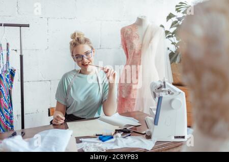 Créateur de mode sur mesure Belle de mesure se situe à dessin en milieu de travail ou de mettre par écrit les résultats après la mesure. Son studio est ensoleillée, pleine de colorf Banque D'Images