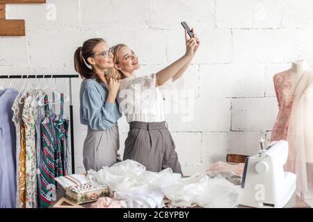 Portrait de deux jeunes femmes prenant tout en selfies travaillant dans l'atelier de couture. Portrait de la mémoire en photo avec son client préféré Banque D'Images
