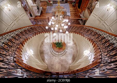 Une vue de haut en bas d'un double escalier dans la grande entrée d'une élégante maison, avec plancher de médaillon, main courante en bois, et broches en fer forgé. Banque D'Images