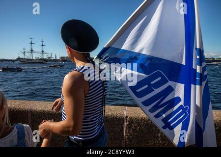 Saint-Pétersbourg, Russie - 26 juillet 2020 UN homme en uniforme de marin et avec le drapeau de Saint-André marche avec un enfant le long de la rive du Palais et regarde le voilier 'Poltava', Qui se trouve dans les eaux de la Neva en formation de parade le jour de la Marine à Saint-Pétersbourg, en Russie. L'inscription sur le drapeau indique « la marine russe » Banque D'Images