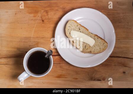 Une tasse blanche avec une cuillère et un café, sur un plateau en bois, une assiette blanche avec une tranche de pain et de beurre faits maison. Nourriture saine, alimentation et cuisine maison. La vue du dessus Banque D'Images