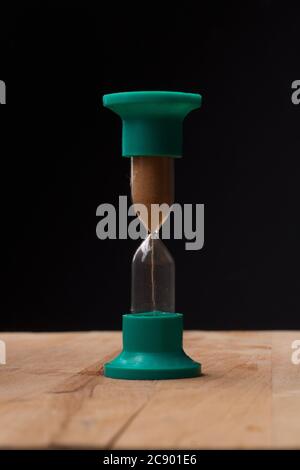 HourGlass en vert se dresse sur une surface en bois. Instantané sur fond noir. Banque D'Images