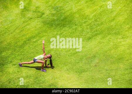 Coureur femme étirant les jambes courir échauffement faire la fente de torsion sur fond de parc d'herbe verte. Bonne entraînement de fille de jogging sur l'été dehors Banque D'Images