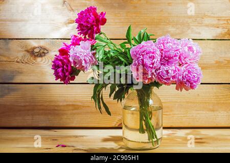 Bouquet de pivoines roses dans une boite transparente sur fond de bois provenant de planches. Banque D'Images