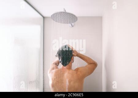 Homme prenant une douche se lavant les cheveux avec le produit de shampooing sous l'eau tombant de la tête de douche de pluie de luxe. Petit matin, hôtel de luxe style de vie Banque D'Images