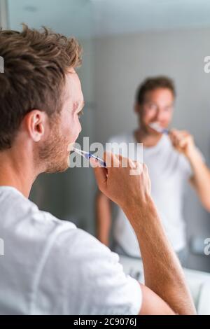 Homme se brossant les dents le matin regardant dans le miroir de salle de bains à l'aide d'une brosse à dents et de dentifrice. Mode de vie à la maison, soins d'hygiène dentaire. Santé bucco-dentaire Banque D'Images