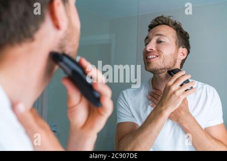 Jeune homme se raser le cou et la ligne de rasoir le matin à l'aide d'un rasoir électrique/tondeuse. Routine du matin style de vie moderne. Beauté masculine modèle 30s Banque D'Images