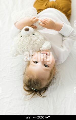 Petite fille souriante couchée au lit avec un jouet ours en peluche Banque D'Images