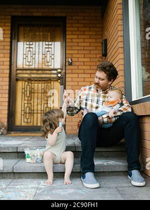 Père avec enfants assis sur le porche Banque D'Images