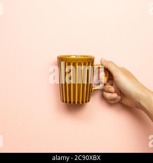 Main femme tenant une tasse vide brune sur fond rose Banque D'Images