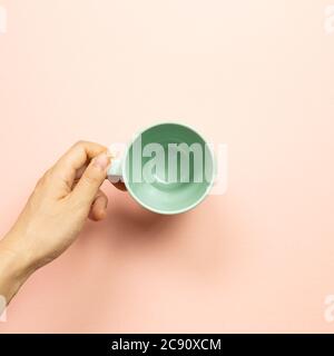 Femme main tenant une tasse vide verte sur fond rose. Vue du dessus Banque D'Images