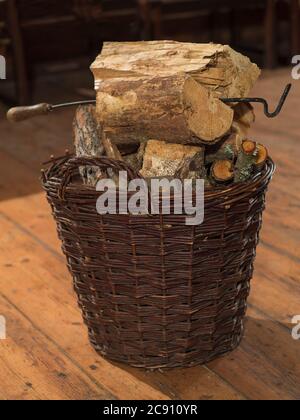 panier en osier plein de bois haché et crochet à feu sur plancher en bois Banque D'Images