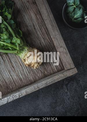 Racine de céleri - apium graveolens - avec feuilles vertes sur plateau en bois grenaille au-dessus avec espace de copie. Photo Dark moody. Banque D'Images