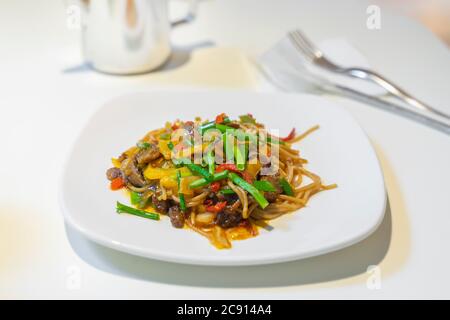 Nouilles asiatiques avec différents légumes et de la viande dans une assiette blanche sur la table gros plan Banque D'Images