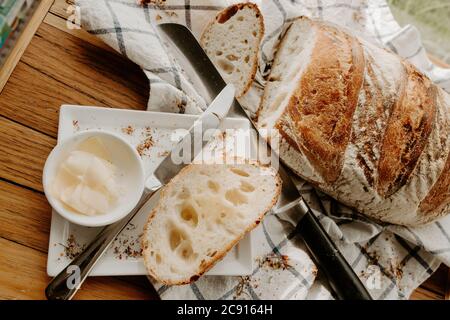 Une tranche de pain sur une assiette blanche avec du beurre et de la pâte à sucre maison refroidissement du pain sur une serviette de thé qui est sur une planche à découper en bois, sauvage Banque D'Images