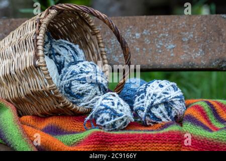 boules de laine bleue et blanche dans un panier en osier sur une couverture tricotée multicolore. Fond naturel. Affiche horizontale avec espace de copie. Fils pour tricot Banque D'Images